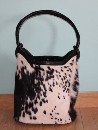 Cowgirl bucket bag in black and white cowhide with leather handles and magnetic closure – front view