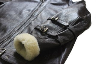 Close-up of buckle strap collar and faux fur trim detail on men's black leather biker jacket