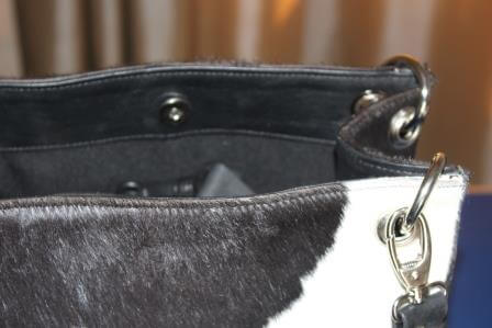 Close-up of dual leather handles and magnetic open-top closure on black white cowhide bucket bag