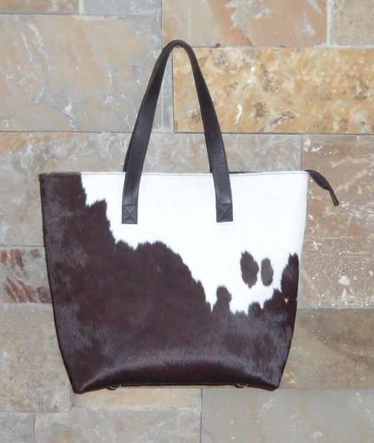 Large brown and white cowhide tote bag with dual leather handles and zipper closure – front view