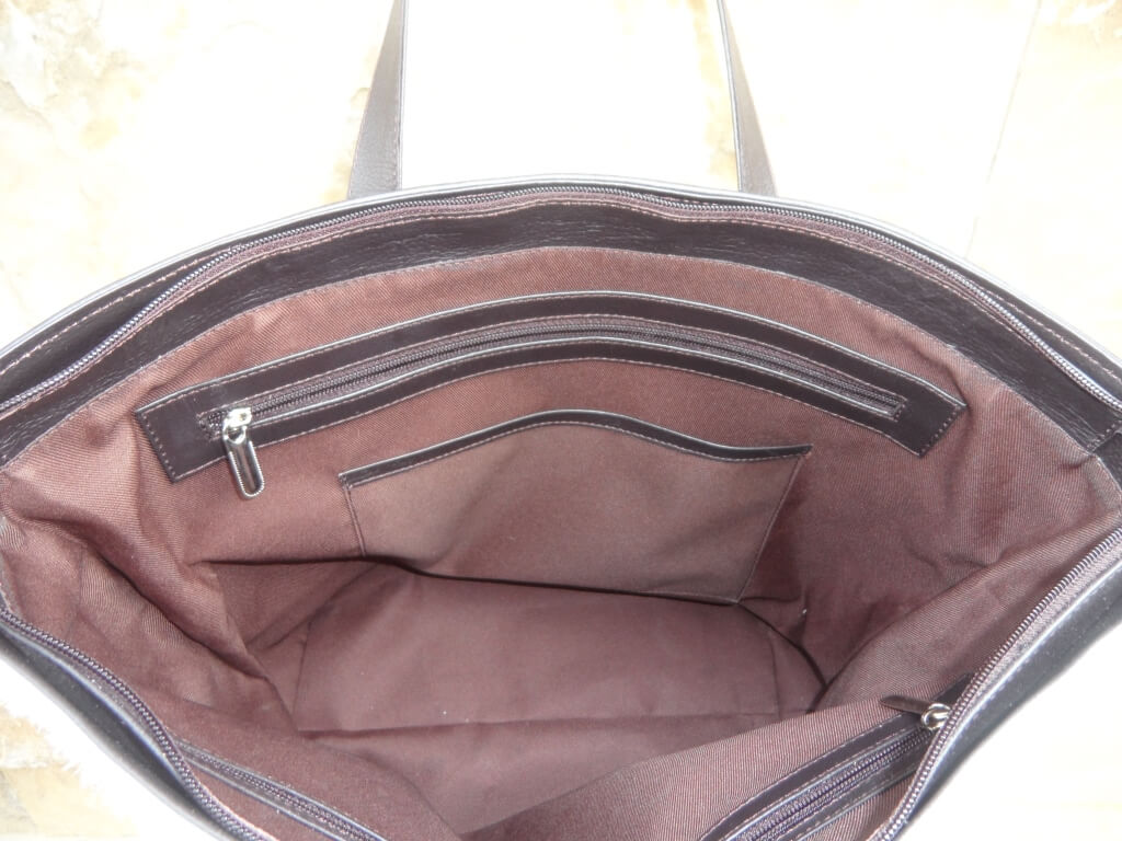 Fully lined interior with zipper and open pockets of large brown white cowhide tote bag